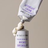 A tube labeled "Aftercare Cream for Fresh Tattoos," 60mL (2 FL. OZ.), squeezes out cream. The background is plain and neutral.